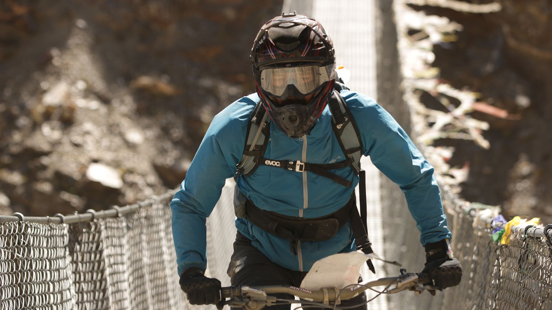 A rider crosses a suspension bridge strung with prayer flags